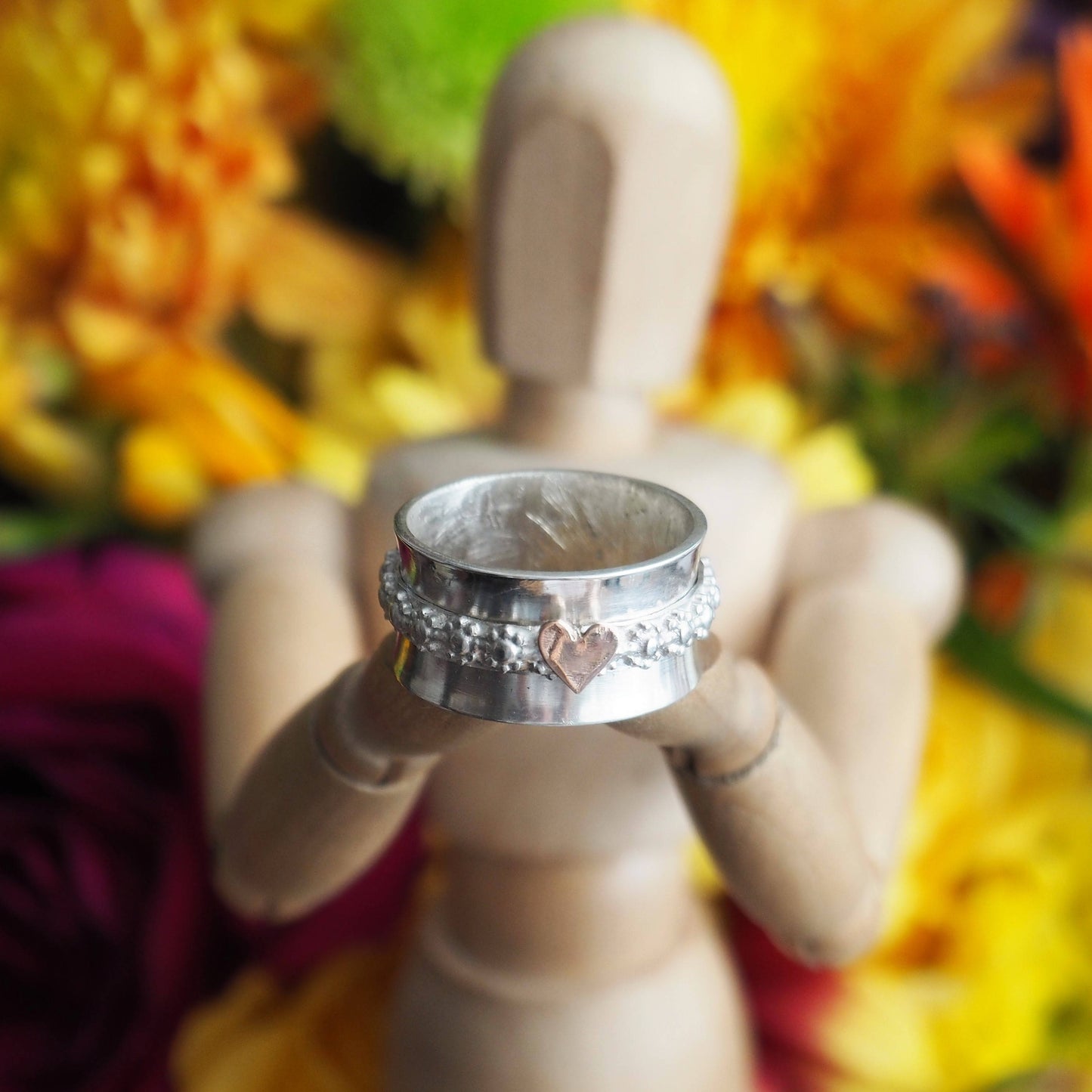 A simple sterling silver ring with handcut 9ct rose gold heart set on narrow daisy flower band spinner ring.