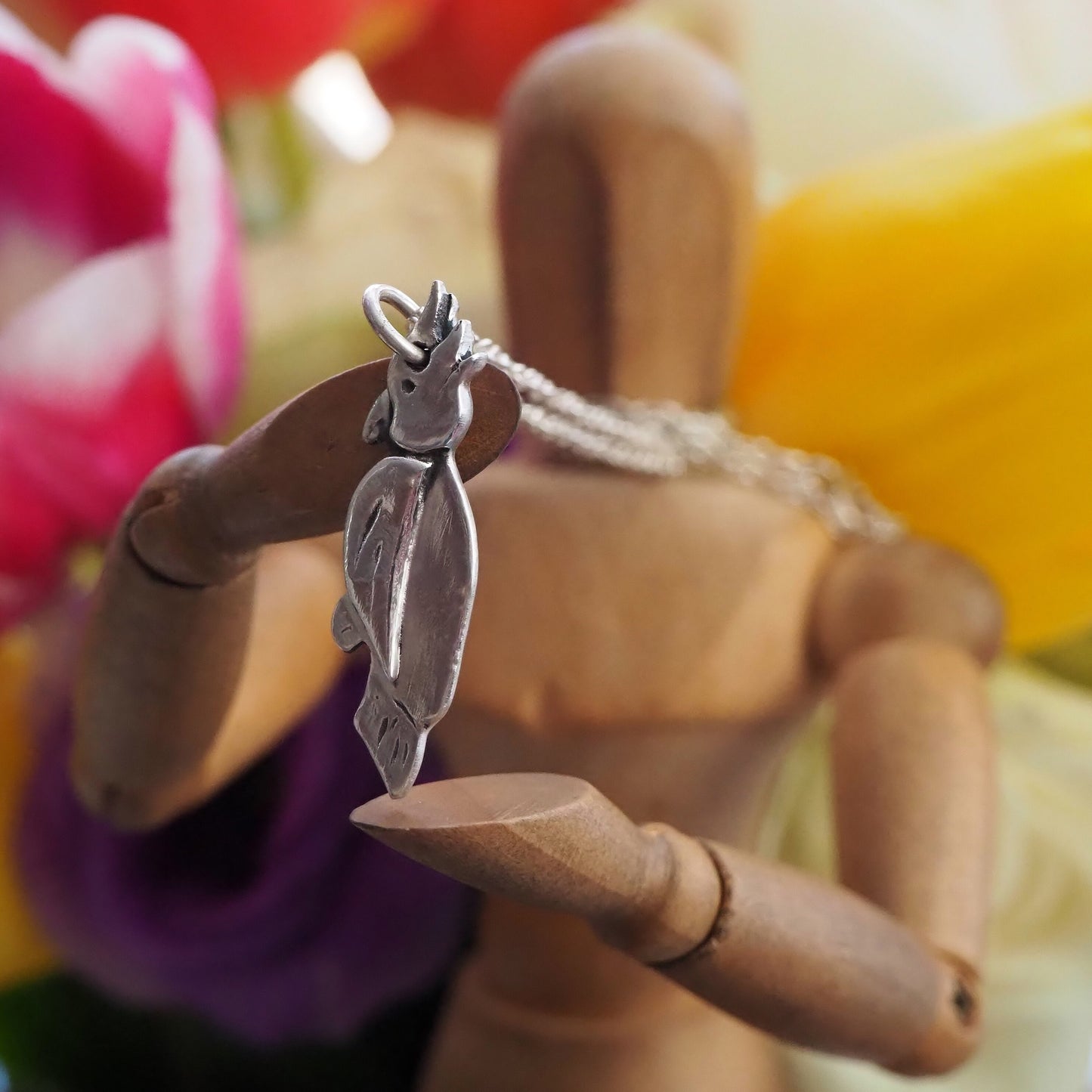 A cute little cockatoo pendant handmade in fine silver hung on a sterling silver chain .