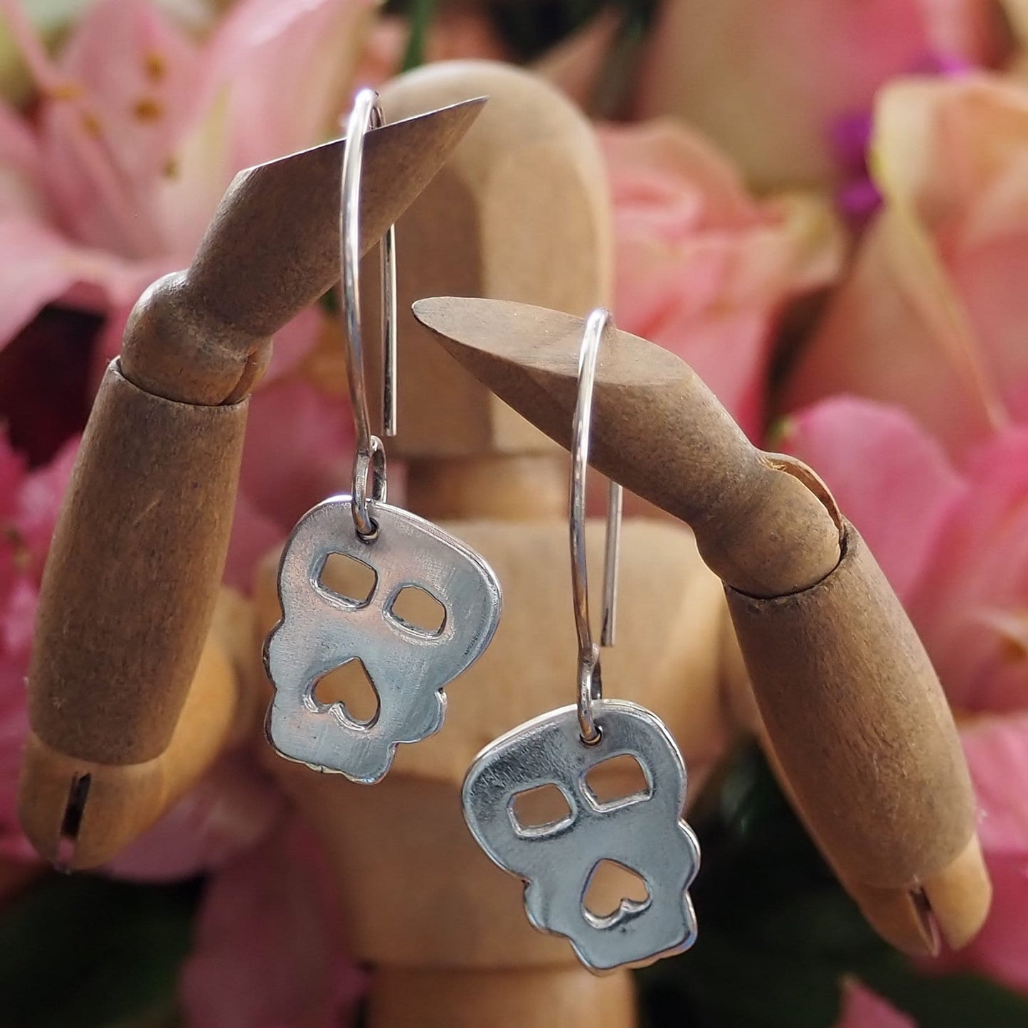 A pair of super simple fine silver handmade Skull earrings hung on sterling silver wires.
