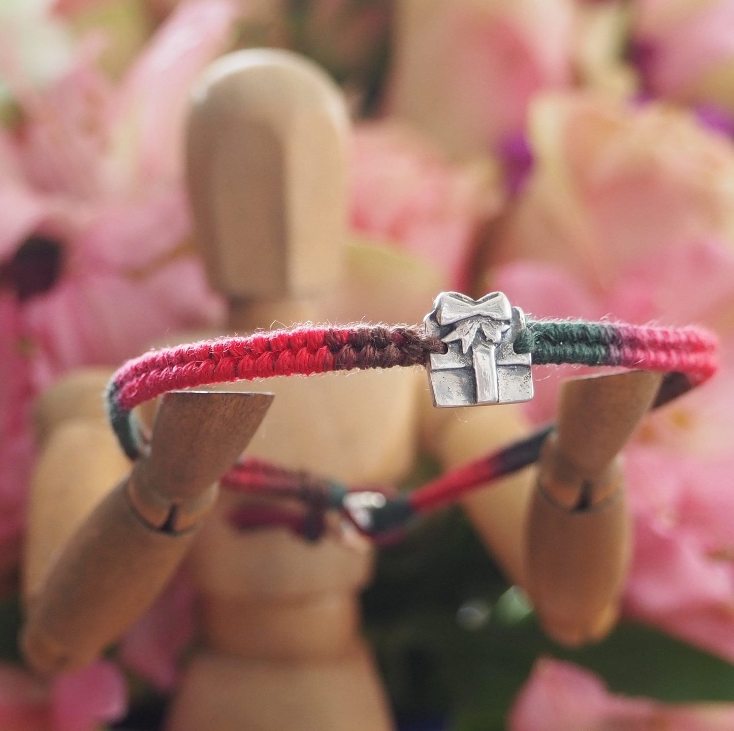 A delightful tiny handmade fine silver parcel on a green/red leather and cotton friendship bracelet with a sterling silver bead clasp.
