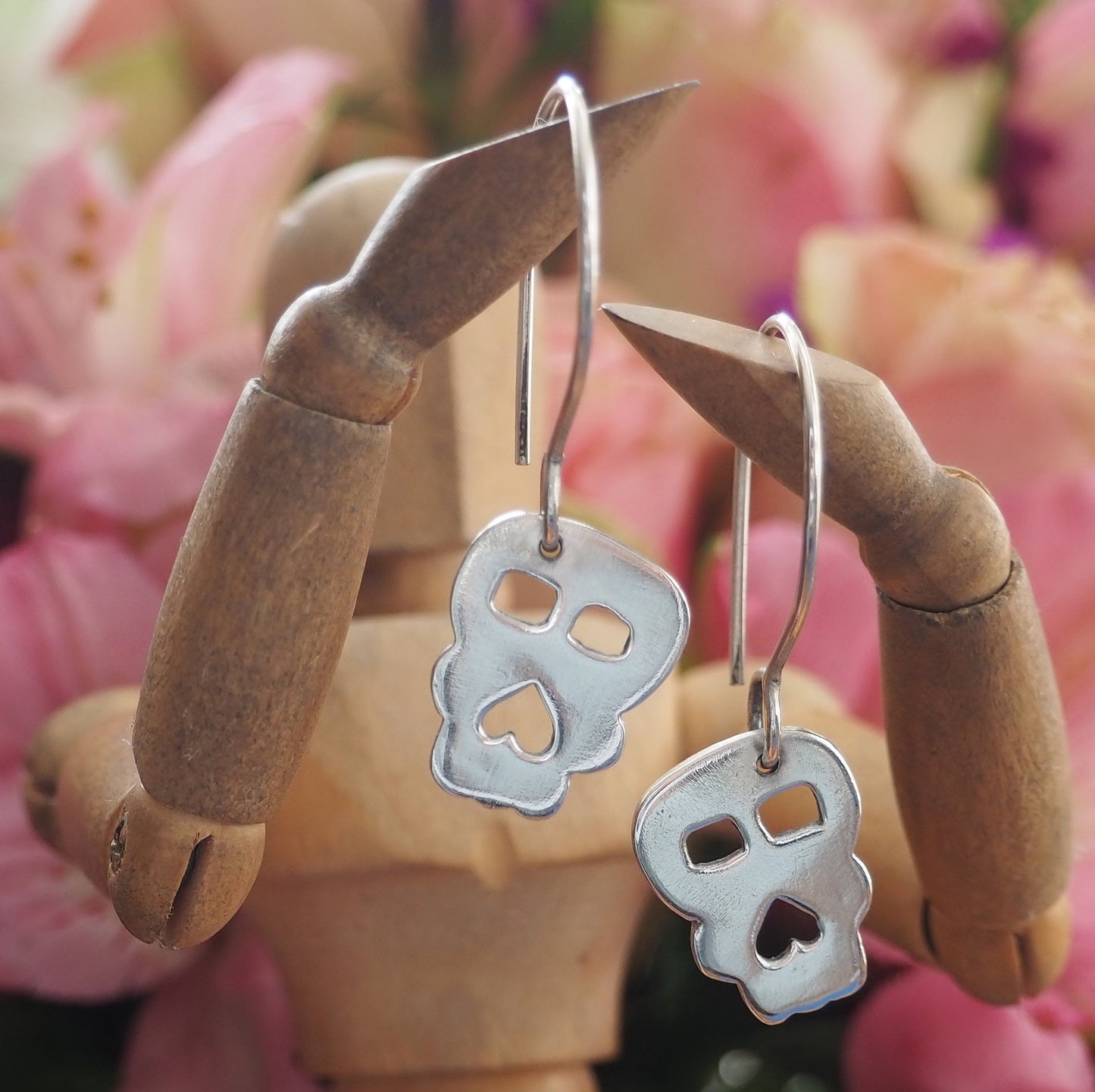 A pair of super simple fine silver handmade Skull earrings hung on sterling silver wires.