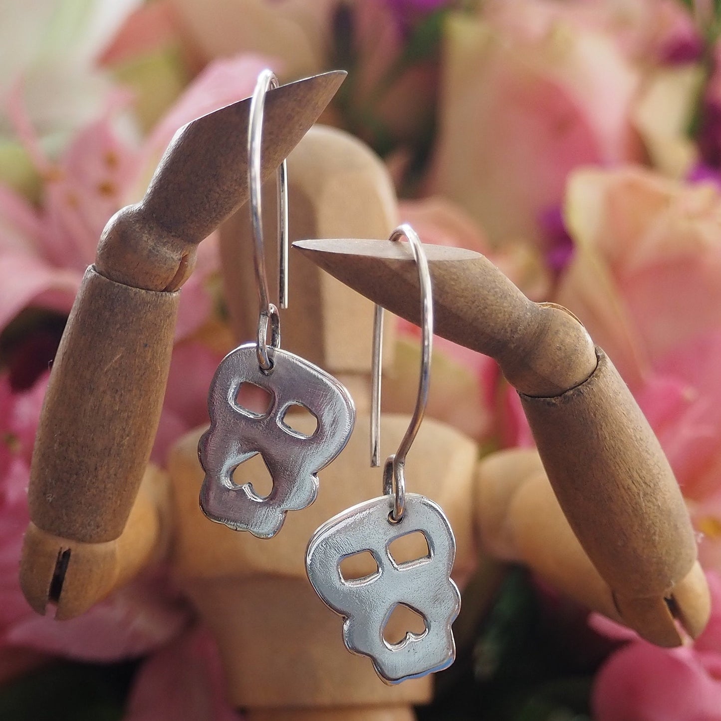 A pair of super simple fine silver handmade Skull earrings hung on sterling silver wires.