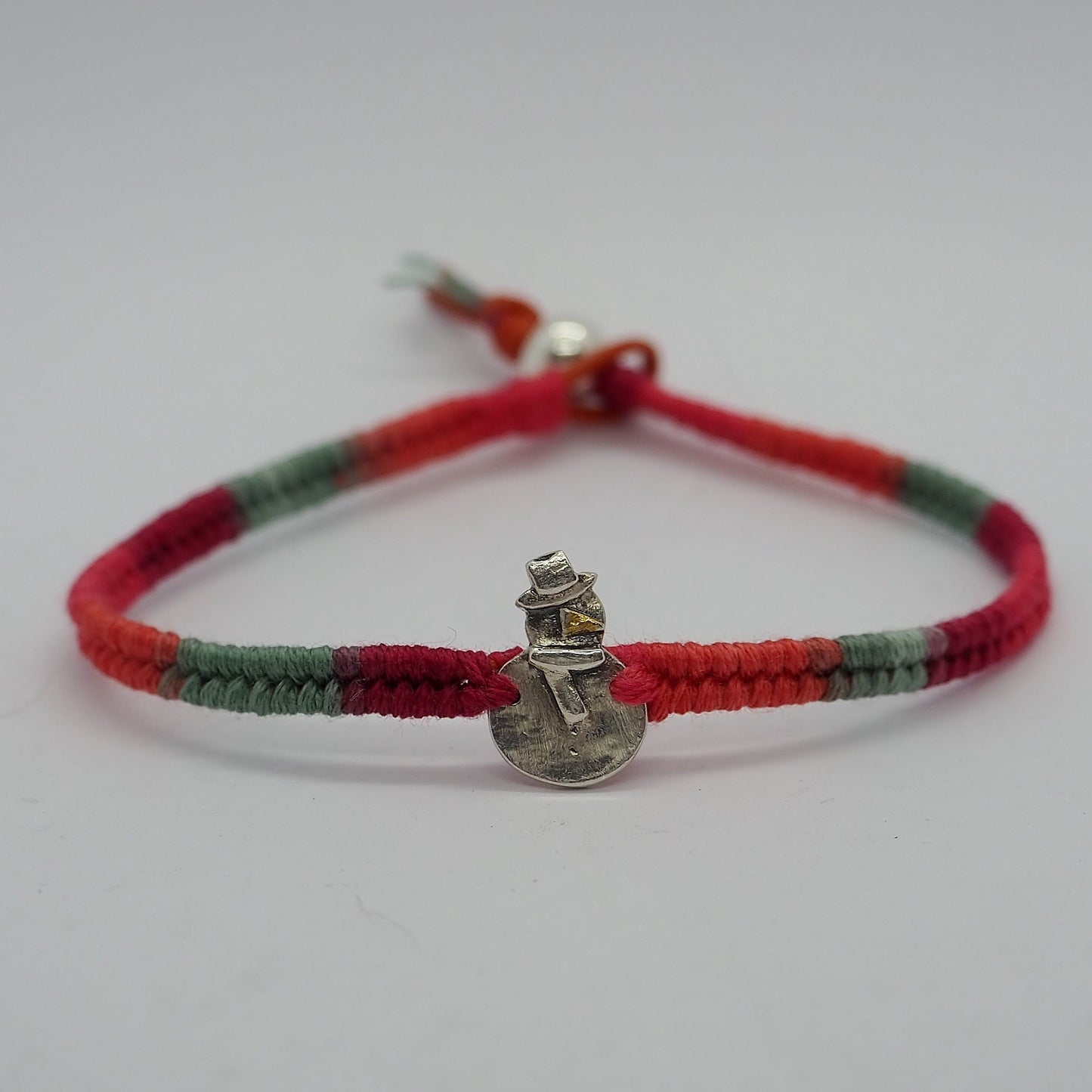 A tiny handmade fine silver snowman with a golden carrot on a green red leather and cotton friendship bracelet with a sterling silver bead…