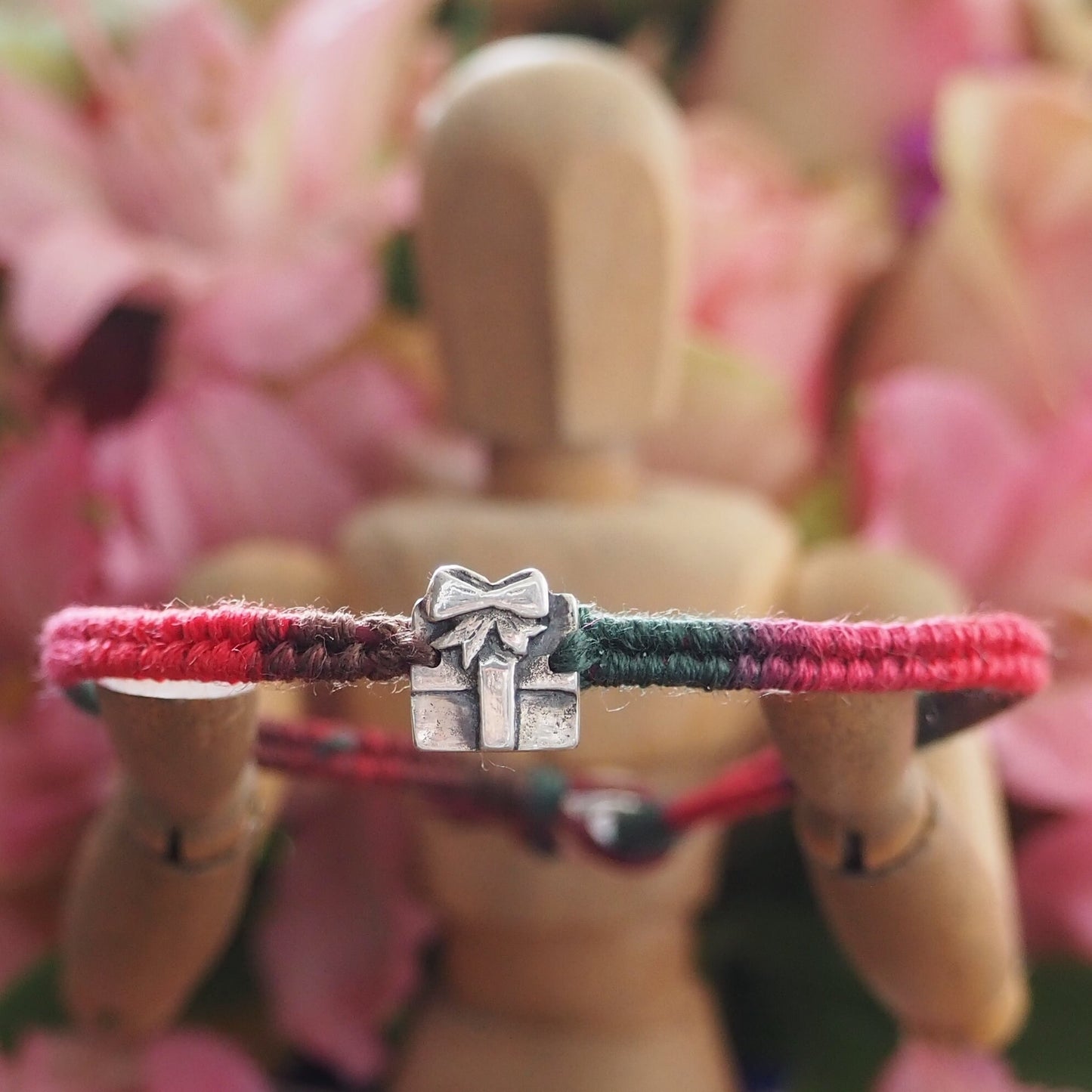 A delightful tiny handmade fine silver parcel on a green/red leather and cotton friendship bracelet with a sterling silver bead clasp.