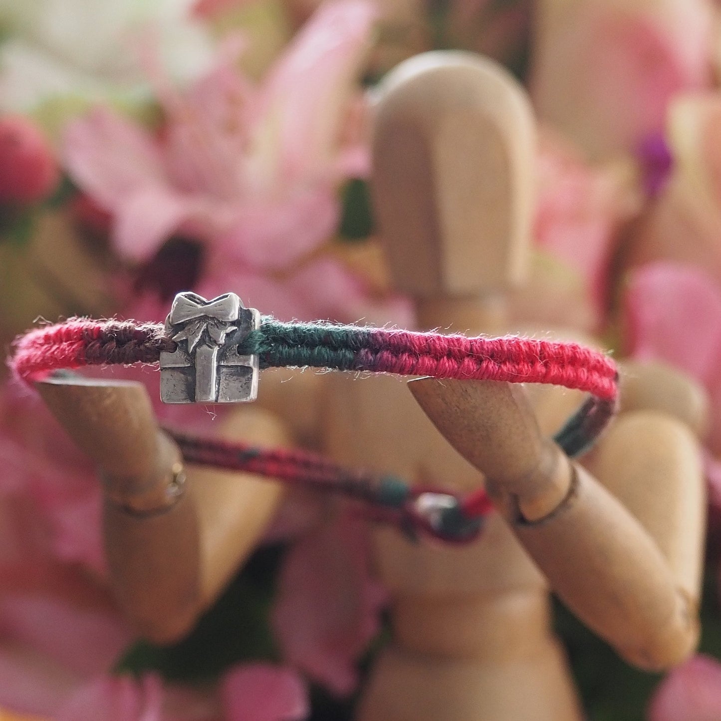 A delightful tiny handmade fine silver parcel on a green/red leather and cotton friendship bracelet with a sterling silver bead clasp.