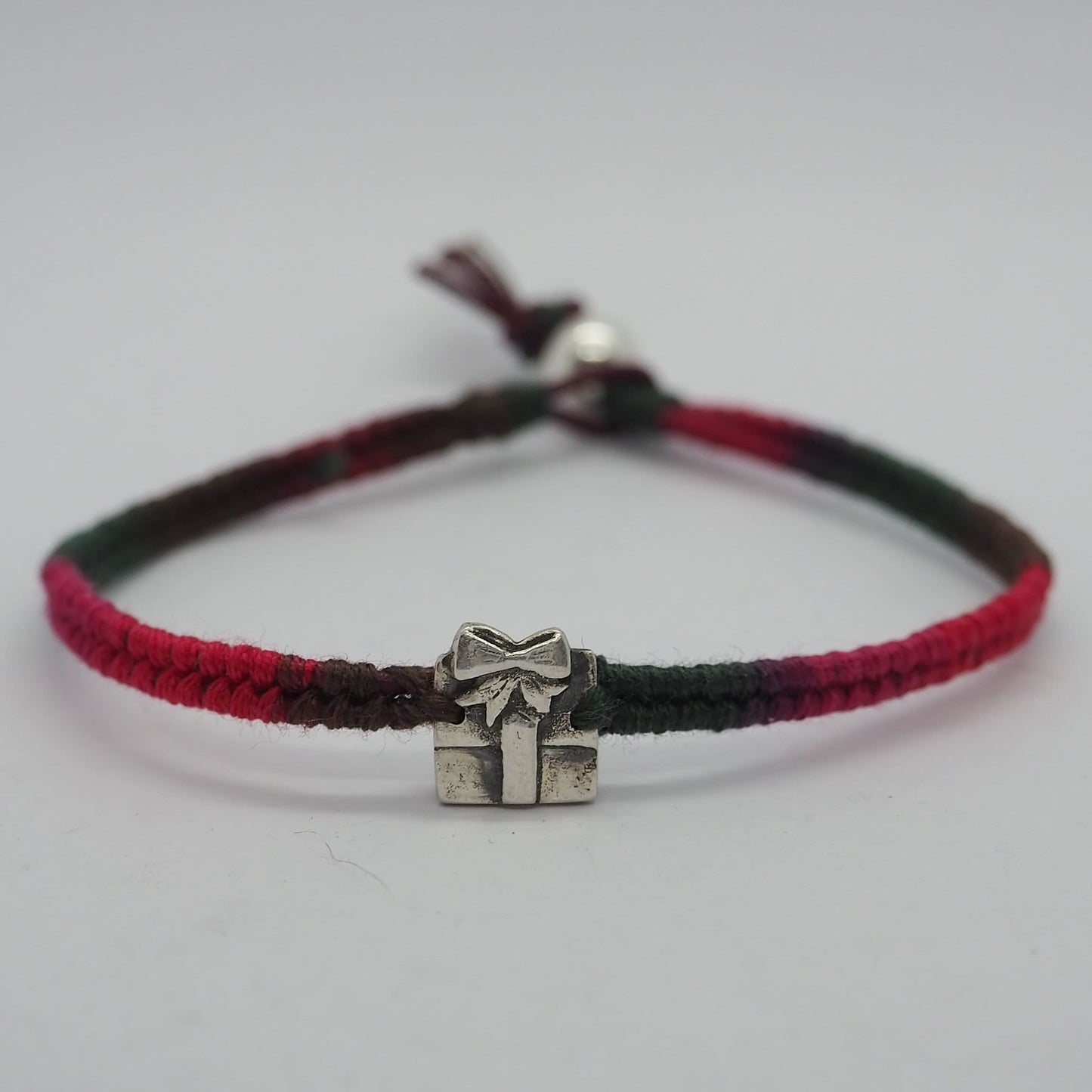 A delightful tiny handmade fine silver parcel on a green/red leather and cotton friendship bracelet with a sterling silver bead clasp.