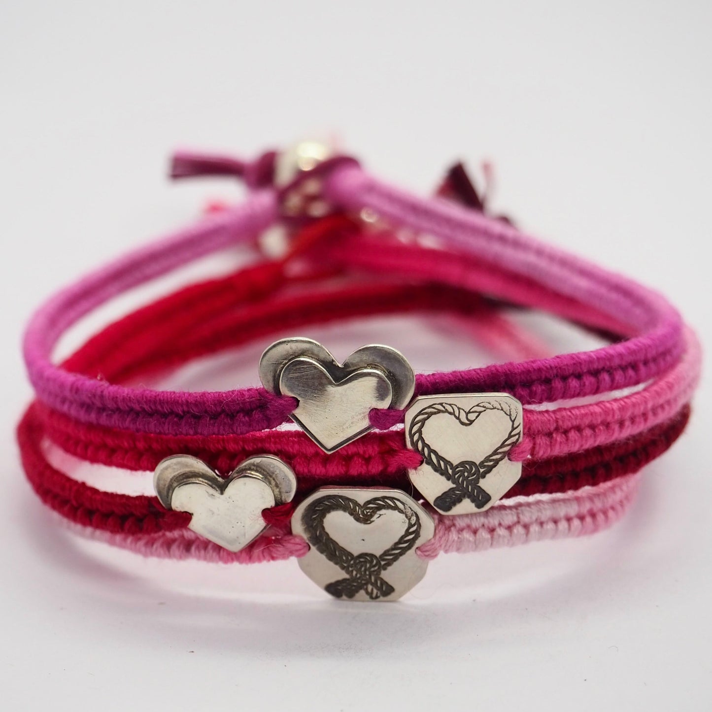 A simple hand cut piece of sterling silver hand stamped with a knotted heart on a lovely vivid pink leather and cotton friendship bracelet.