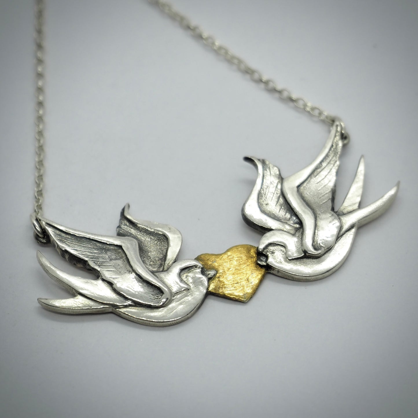 A gorgeous handmade fine silver love birds and gold heart necklace inspired by tattoos hung on a sterling silver chain.