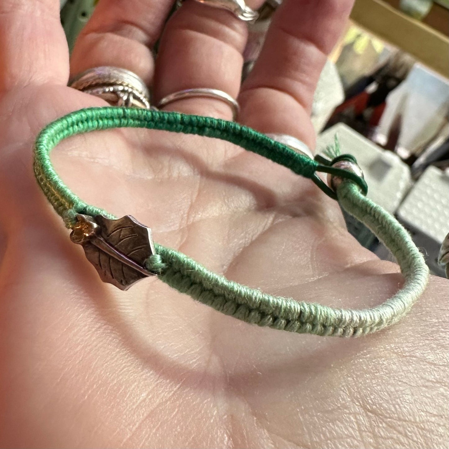 A delightful handmade fine silver holly leaf with gold berries on a green leather, cotton and sterling silver woven friendship bracelet…