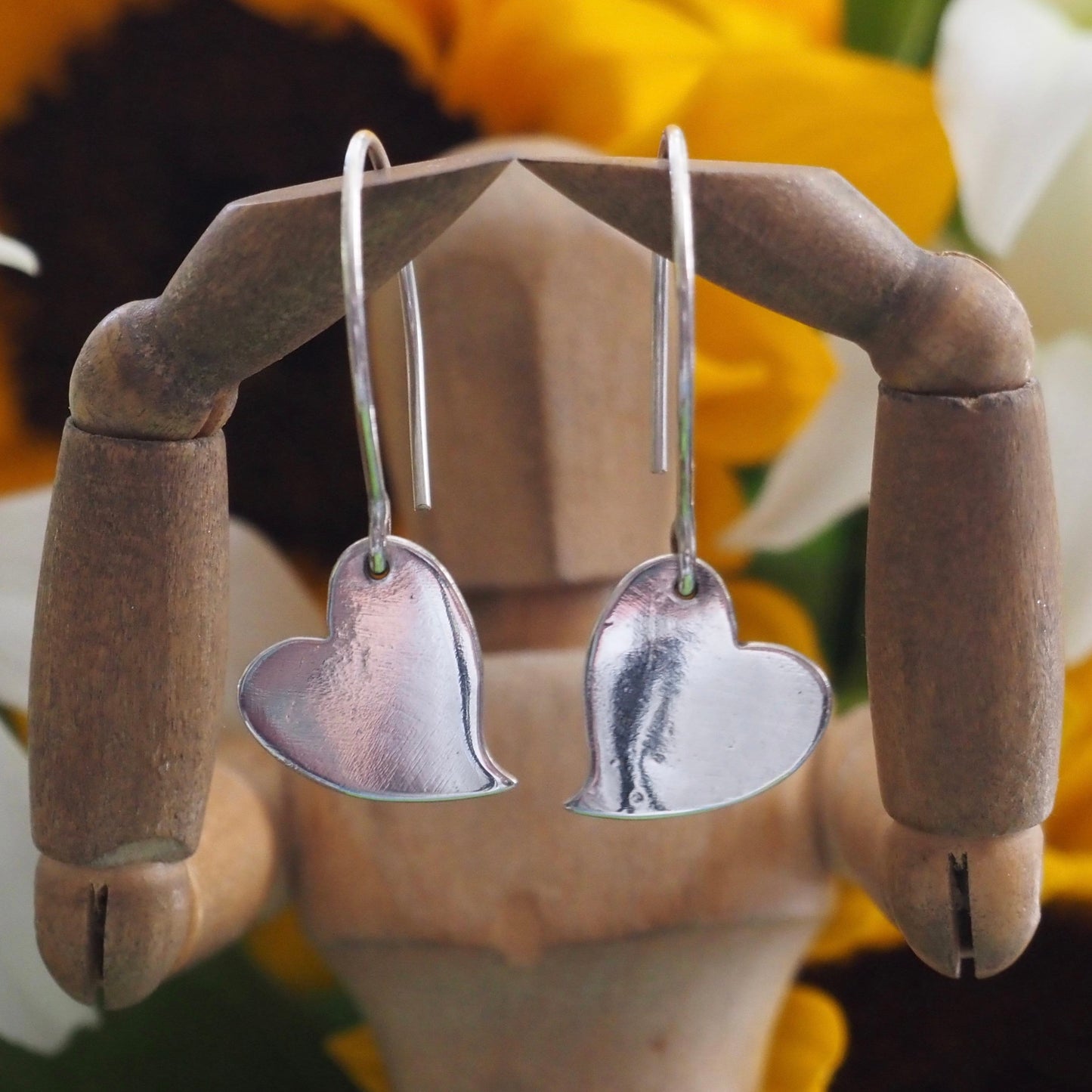 A pair of simple fine silver kicking heart earrings on handmade sterling silver wires.