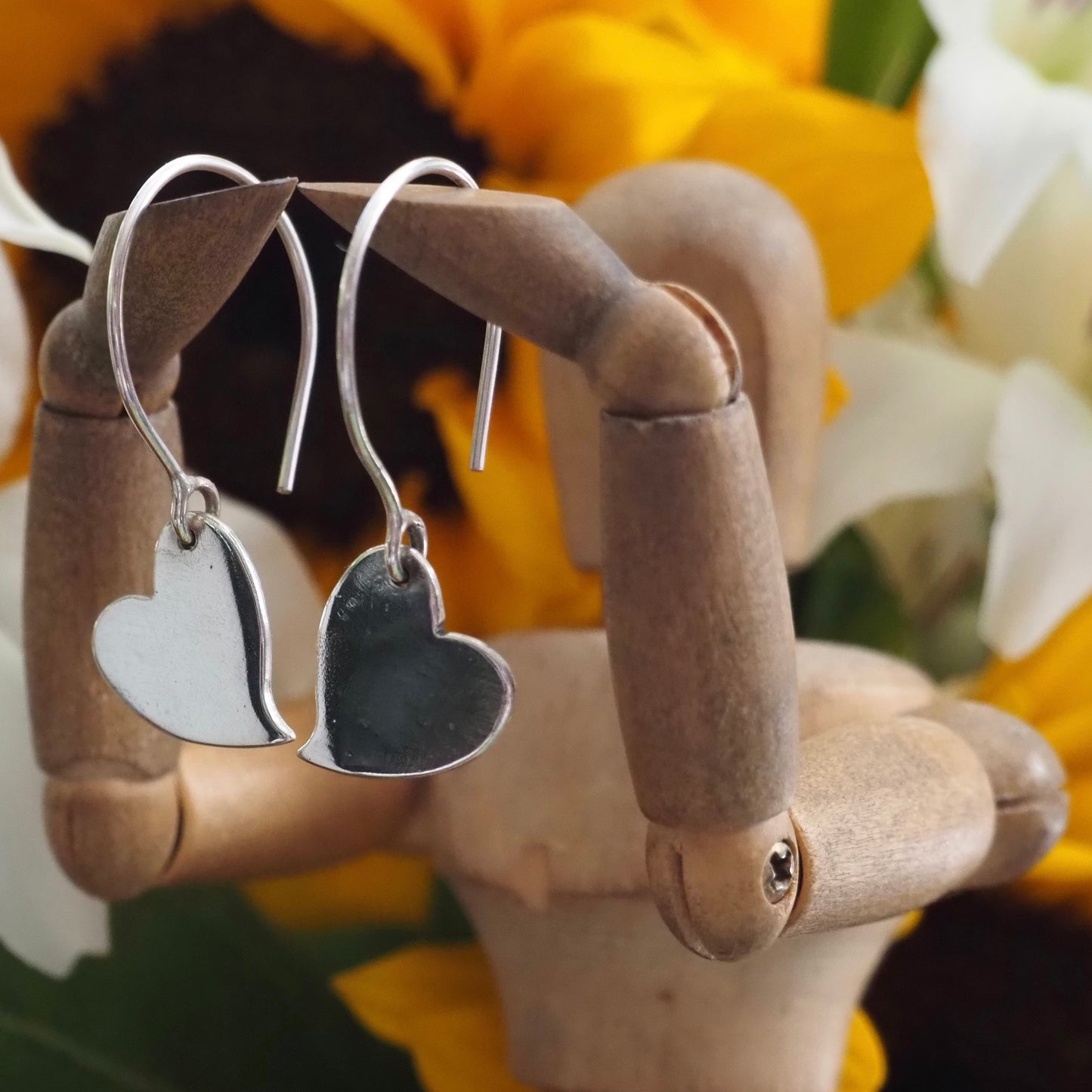 A pair of simple fine silver kicking heart earrings on handmade sterling silver wires.