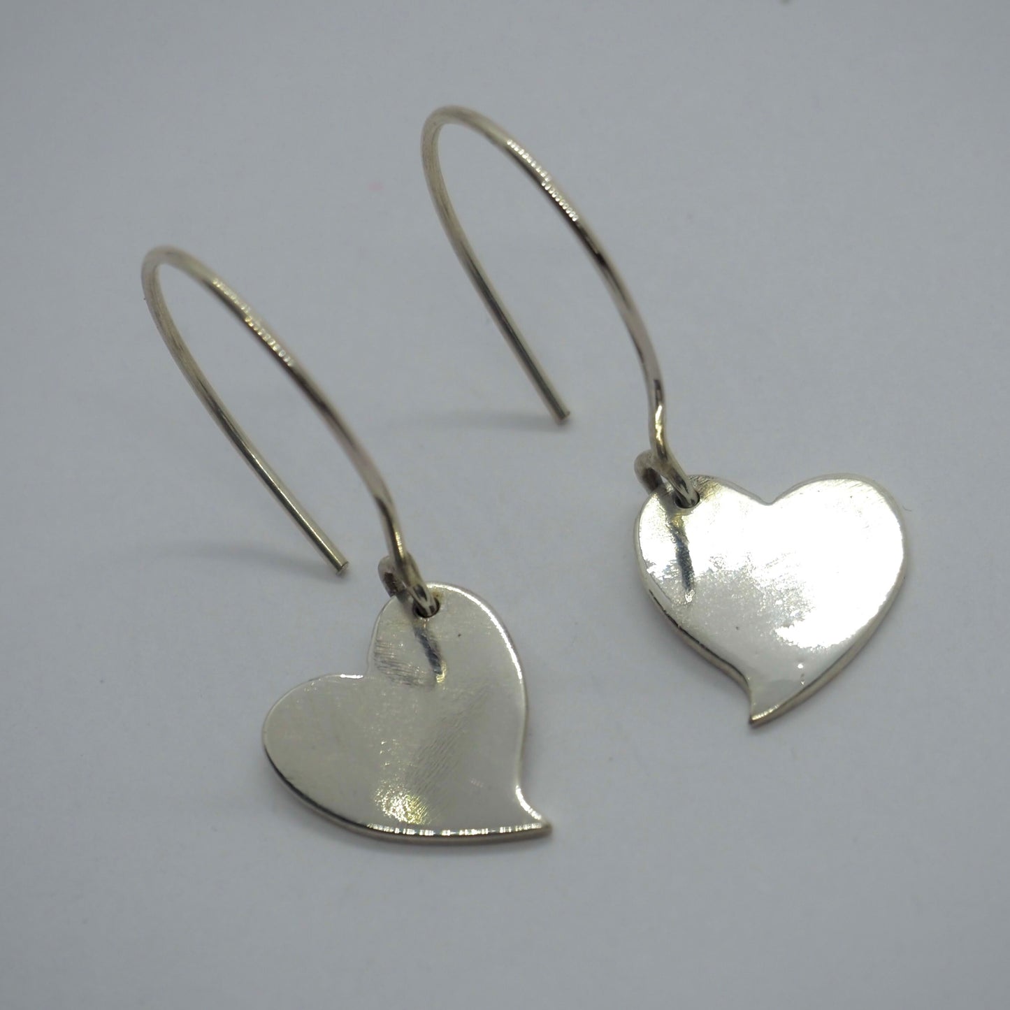 A pair of simple fine silver kicking heart earrings on handmade sterling silver wires.