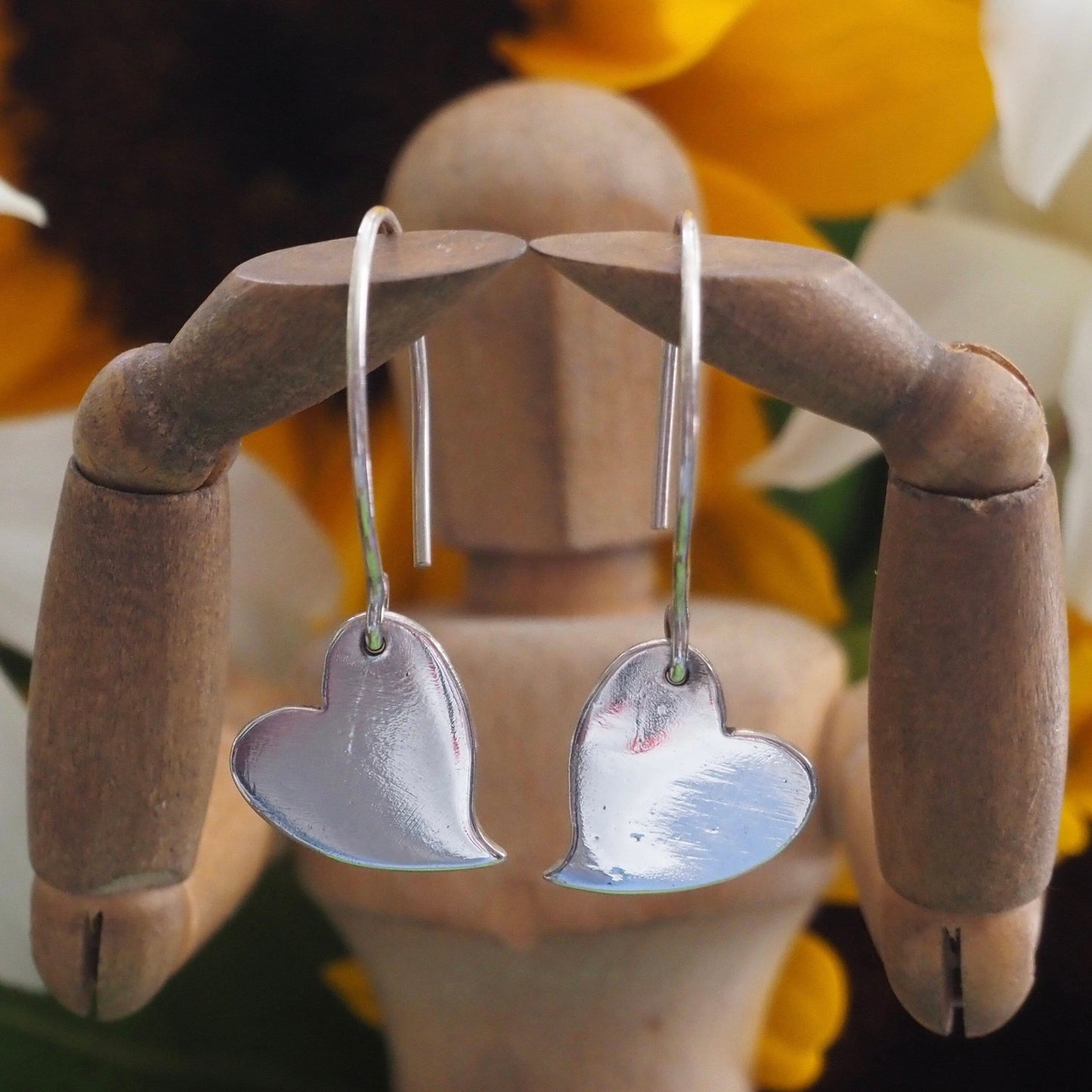 A pair of simple fine silver kicking heart earrings on handmade sterling silver wires.