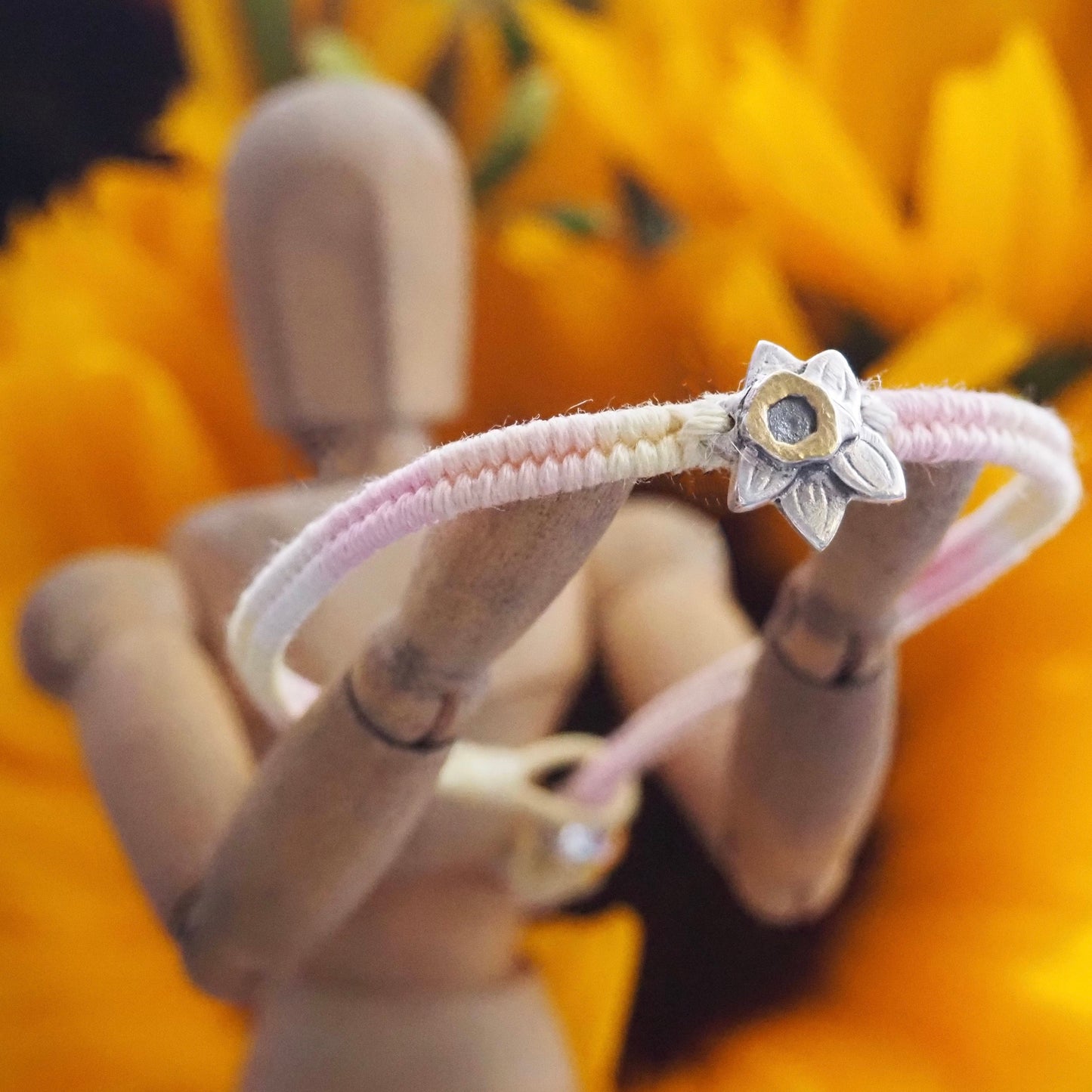 A hand made fine silver spring daffodil highlighted with gold on a peachy pinks leather, sterling silver and cotton friendship bracelet.