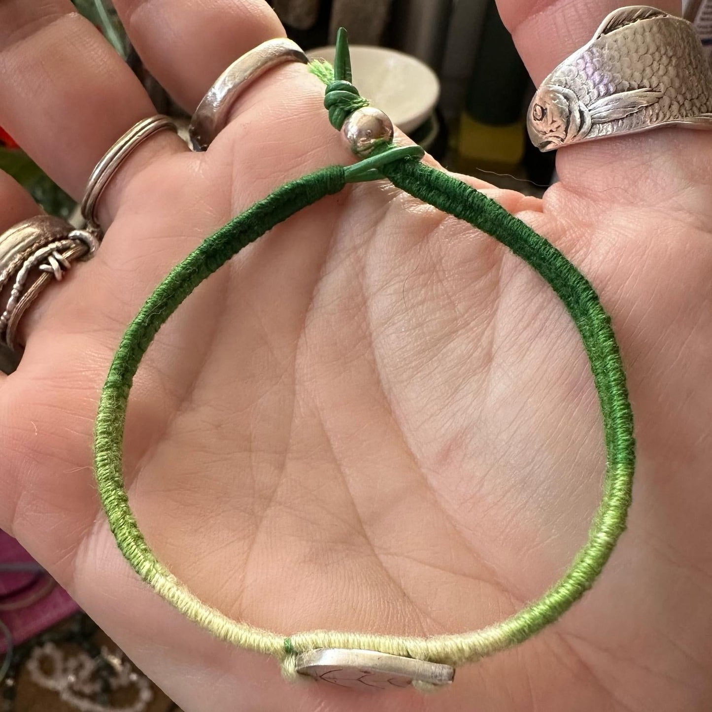 A lovely simple fine silver leaf on a beautiful green leather, sterling silver and cotton woven charm bracelet.