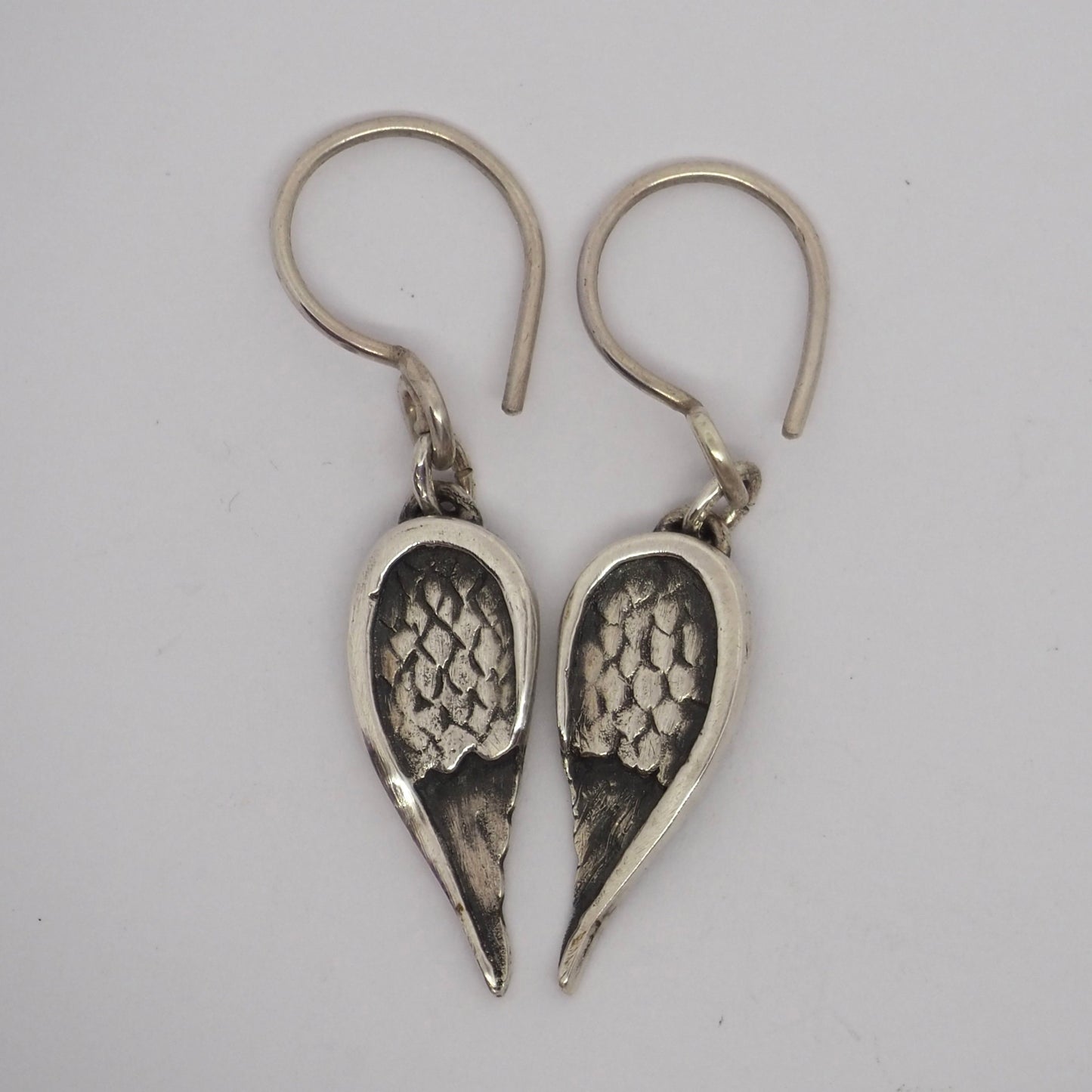 A pretty pair of fine silver angel wing earrings hung on handmade sterling silver loops.