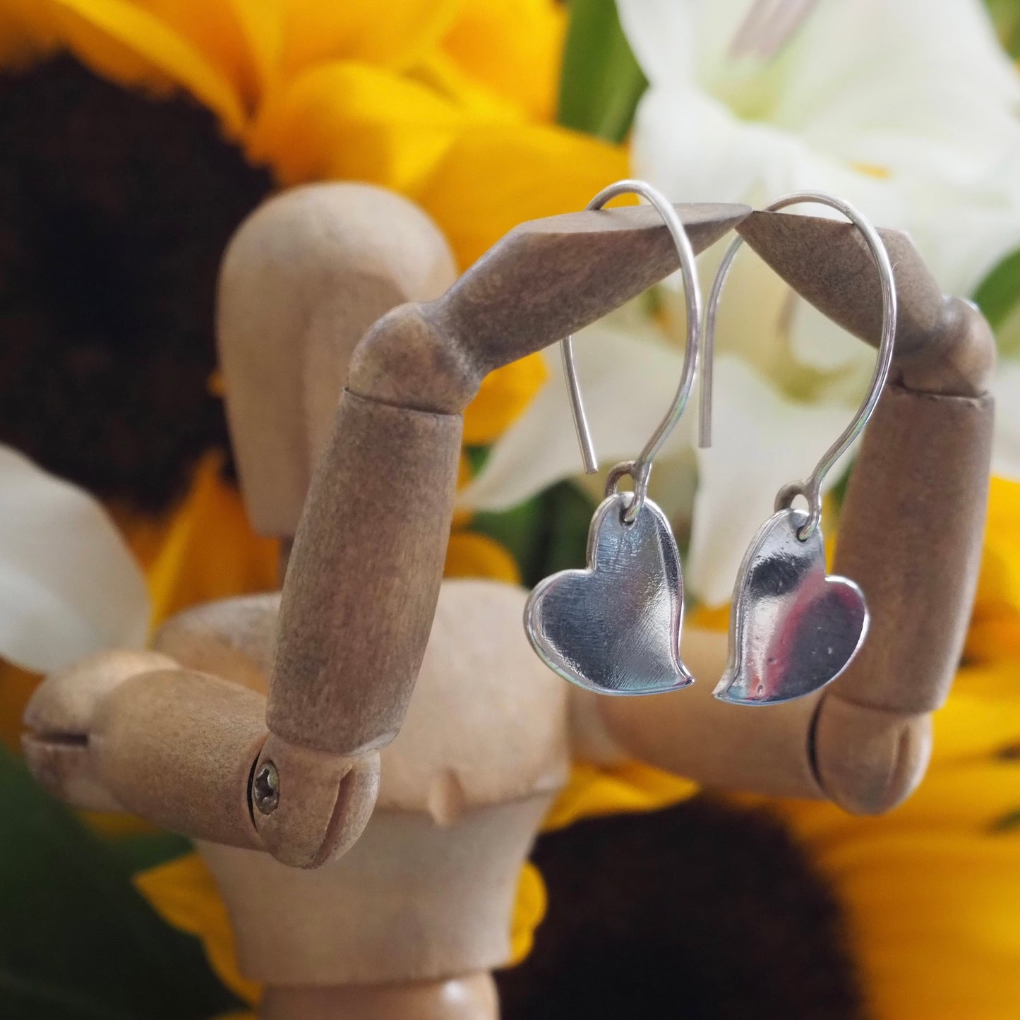 A pair of simple fine silver kicking heart earrings on handmade sterling silver wires.