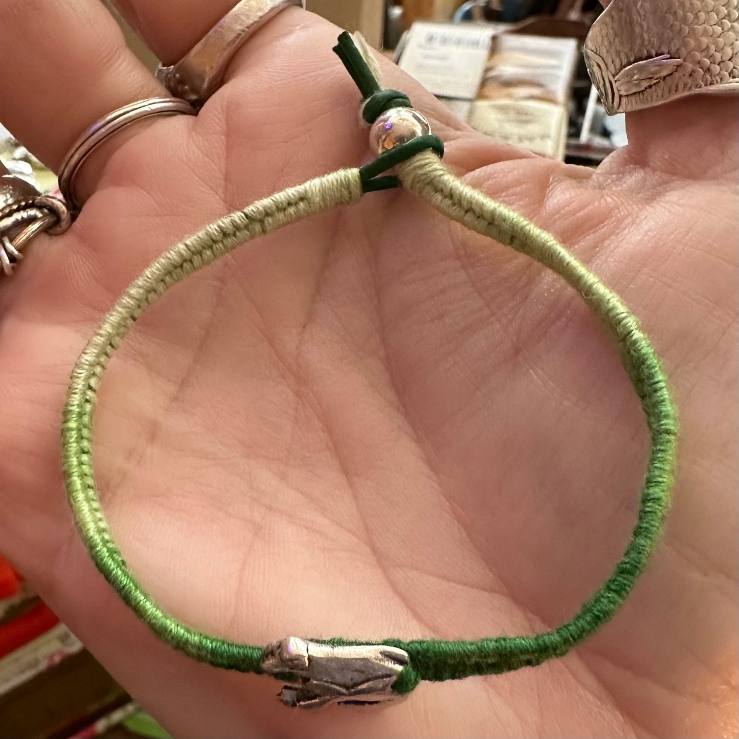 A gorgeous tiny fine silver frog on a green leather, cotton and sterling silver woven charm bracelet.
