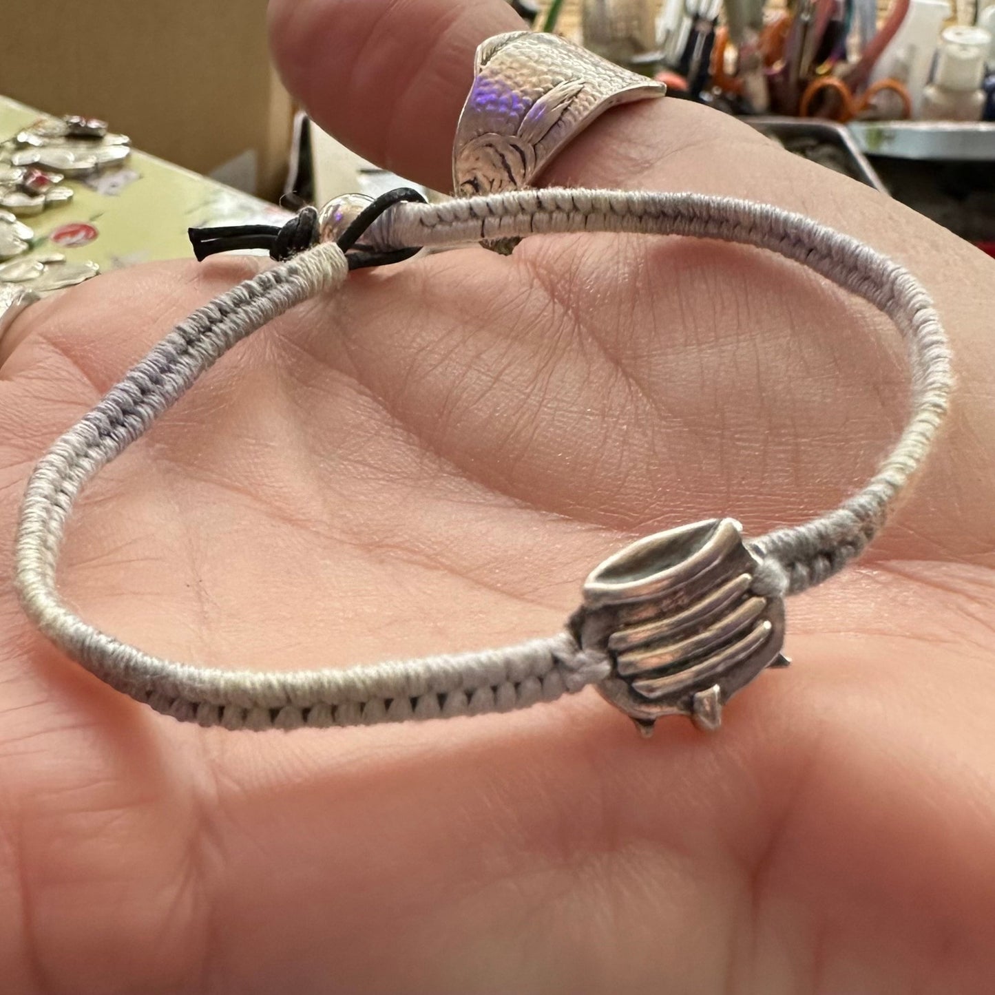 A spooky little handmade fine silver witches cauldron on a soft greys cotton, leather and sterling silver woven charm bracelet.