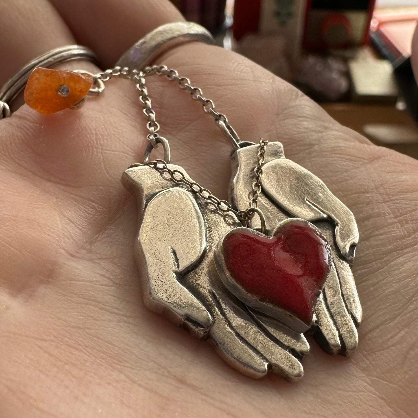 A wonderful pair of chunky fine silver hands cupping a red enamelled heart attached by 9ct gold chain hung on a sterling silver chain.