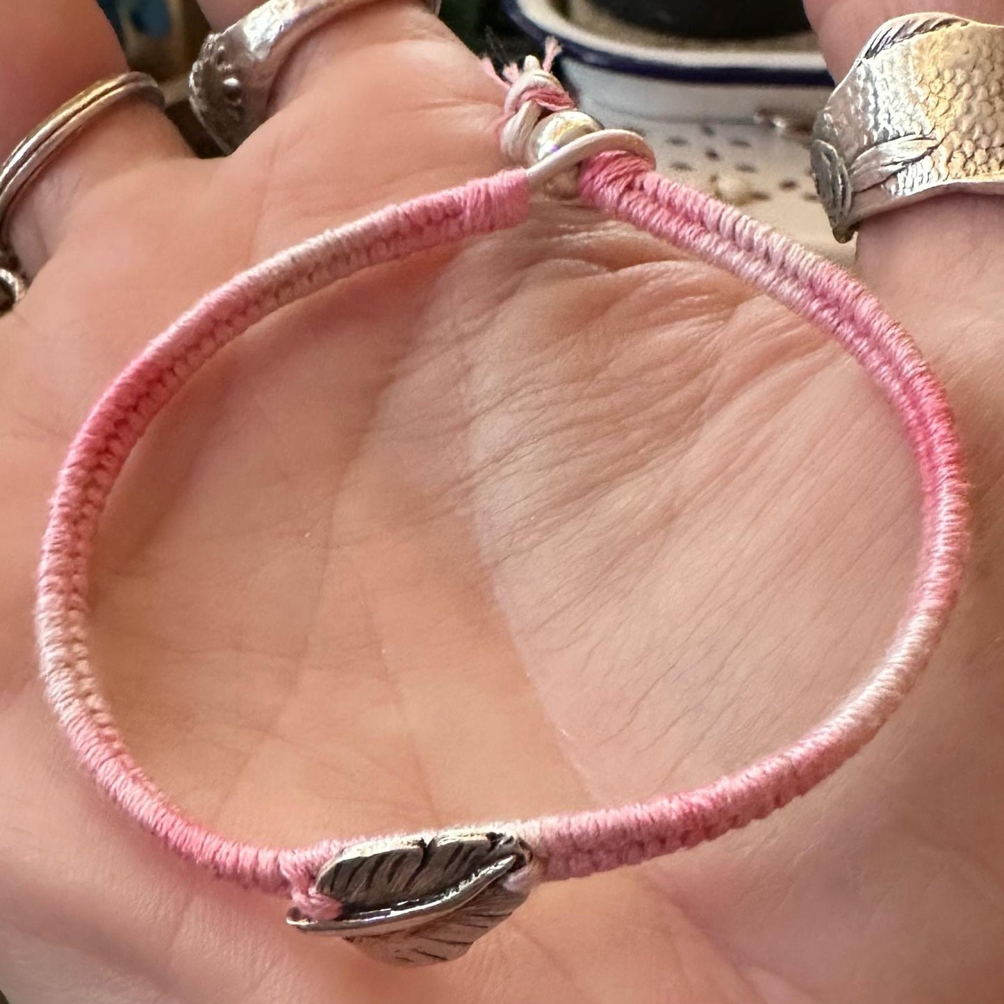 A delightful handmade fine silver feather on a shades of dusty pink friendship bracelet in leather, sterling silver and cotton.