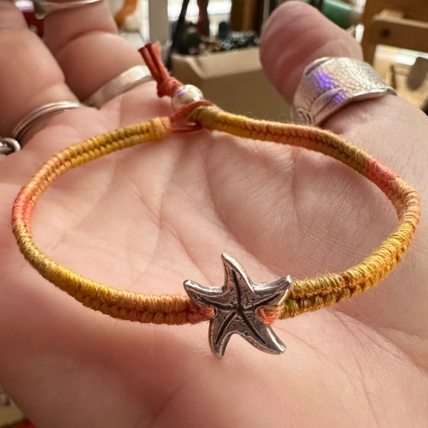 A cute unique tiny fine silver starfish on a beautiful orange leather, sterling silver and cotton woven charm bracelet.