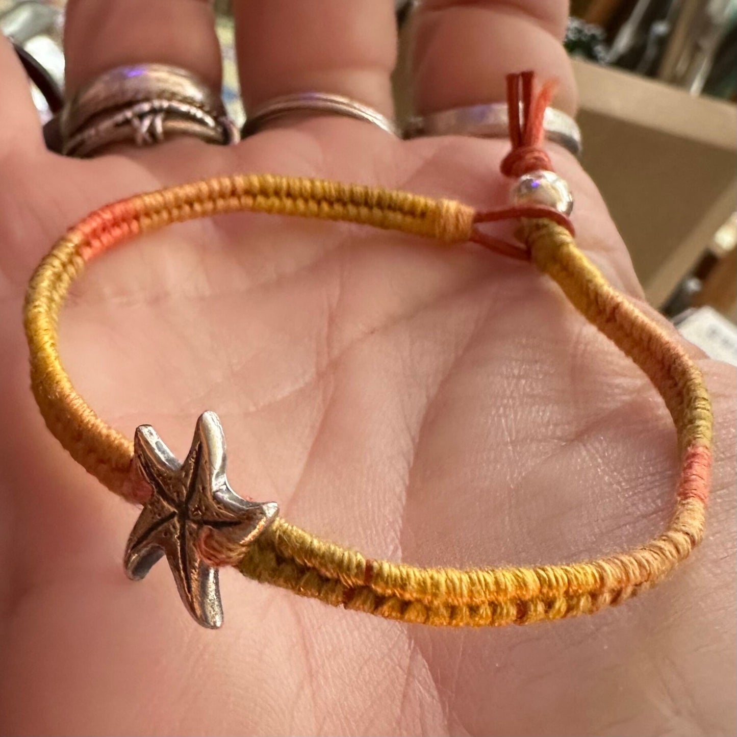A cute unique tiny fine silver starfish on a beautiful orange leather, sterling silver and cotton woven charm bracelet.