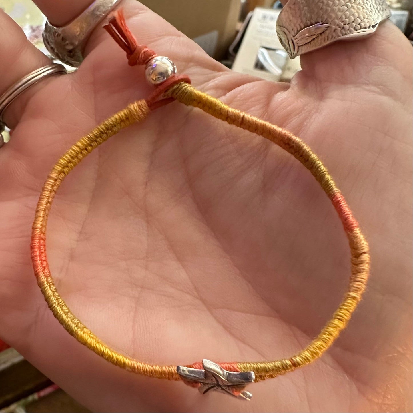 A cute unique tiny fine silver starfish on a beautiful orange leather, sterling silver and cotton woven charm bracelet.