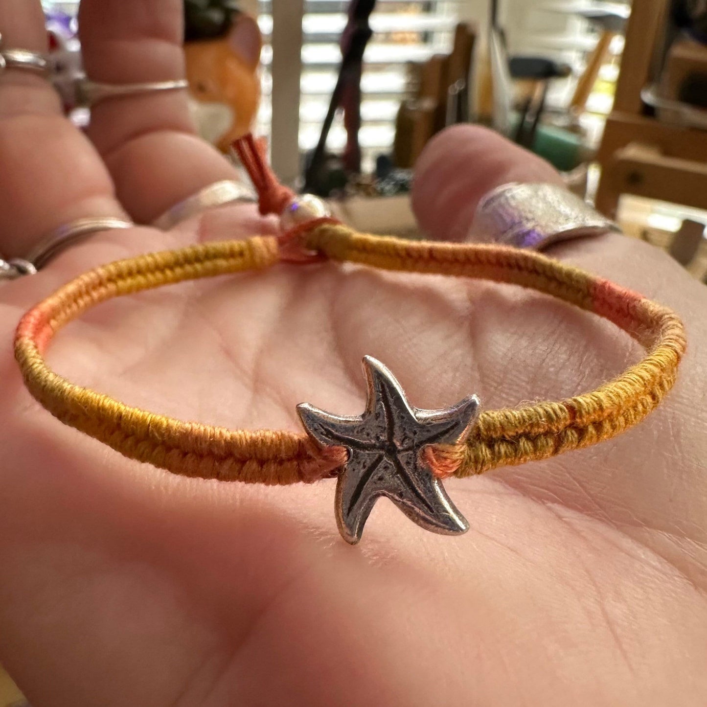 A cute unique tiny fine silver starfish on a beautiful orange leather, sterling silver and cotton woven charm bracelet.