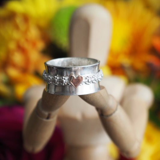 A simple sterling silver ring with handcut 9ct rose gold heart set on narrow daisy flower band spinner ring.