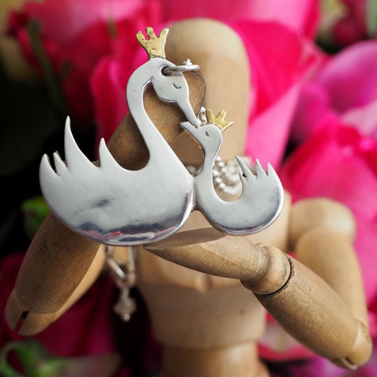 A gorgeous mother and child handmade swans in fine silver wearing golden crowns on a sterling silver chain.