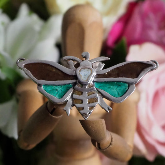 A gorgeous moth pendant, handmade in fine silver and hand enamelled with a skull motif, hung on a sterling silver chain.