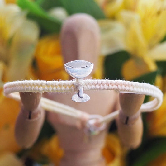 A cute peachy cream friendship bracelet with a handmade fine silver champagne coupe on cotton and leather with a sterling silver bead