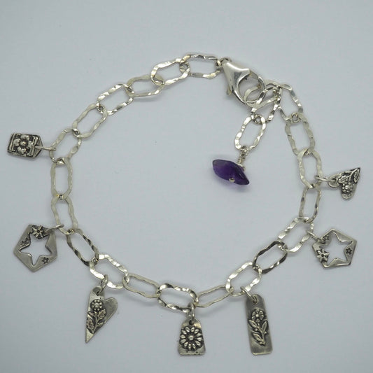 A gorgeous delicate charm bracelet with recycled sterling silver hand made charms on a hammered loop chain finished with an amethyst.