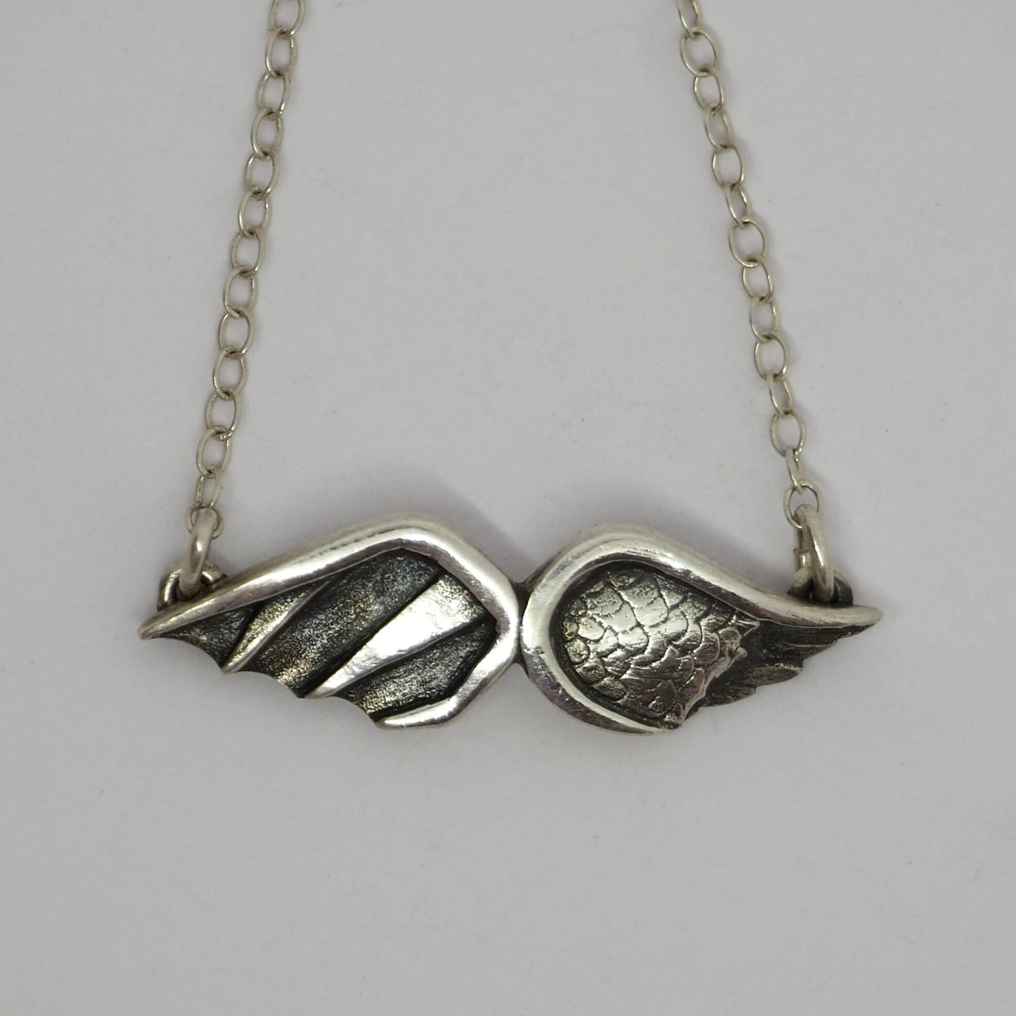 A gorgeous handmade fine silver Angel and Devil Wings necklace hung on a sterling silver chain.