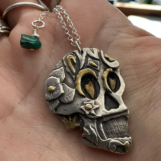 A gorgeous handmade, unique fine silver sugar skull pendant with a gold details hanging on a sterling silver chain.