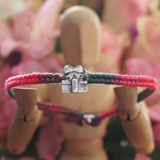 A delightful tiny handmade fine silver parcel on a green/red leather and cotton friendship bracelet with a sterling silver bead clasp.