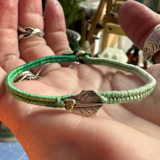 A delightful handmade fine silver holly leaf with gold berries on a green leather, cotton and sterling silver woven friendship bracelet…