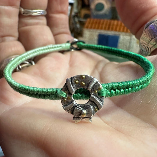 A delightful handmade fine silver wreath with gold decorations on a green leather, cotton and sterling silver woven friendship bracelet