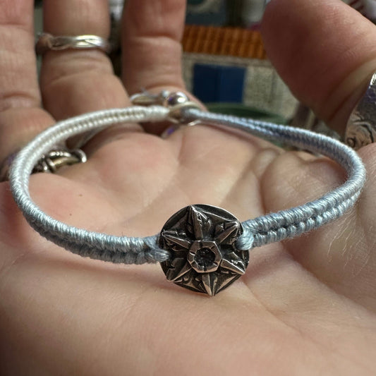 A delicate handmade fine silver snowflake on a cool blue leather, cotton and sterling silver woven bracelet.