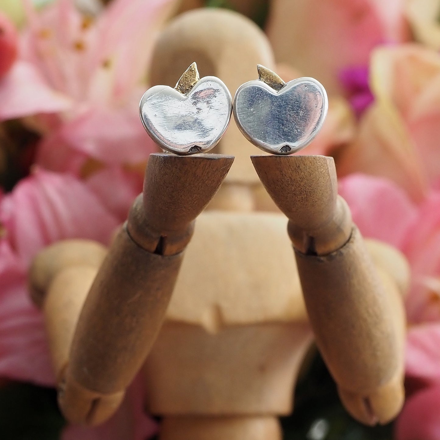 A pair of tiny fine silver apple stud earrings on sterling silver posts enhanced with little gold leaves.