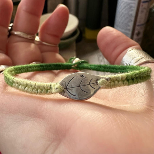 A lovely simple fine silver leaf on a beautiful green leather, sterling silver and cotton woven charm bracelet.