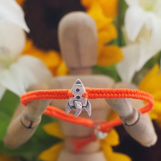 A cute unique tiny fine silver rocket on a beautiful orange leather, sterling silver and cotton woven charm bracelet.