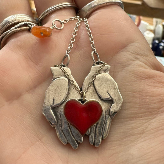 A wonderful pair of chunky fine silver hands cupping a red enamelled heart attached by 9ct gold chain hung on a sterling silver chain.