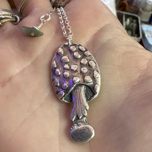 A beautiful handmade fine silver toadstool mushroom pendant hung on a sterling silver chain.