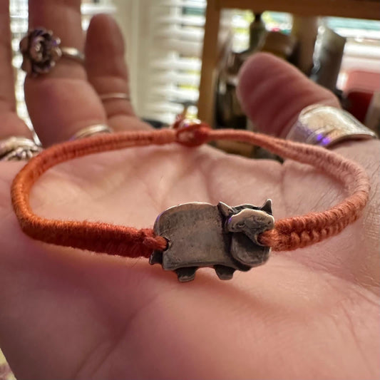 A cute little handmade fine silver highland cow on a vivid browny/orange leather, cotton and sterling silver woven friendship bracelet…